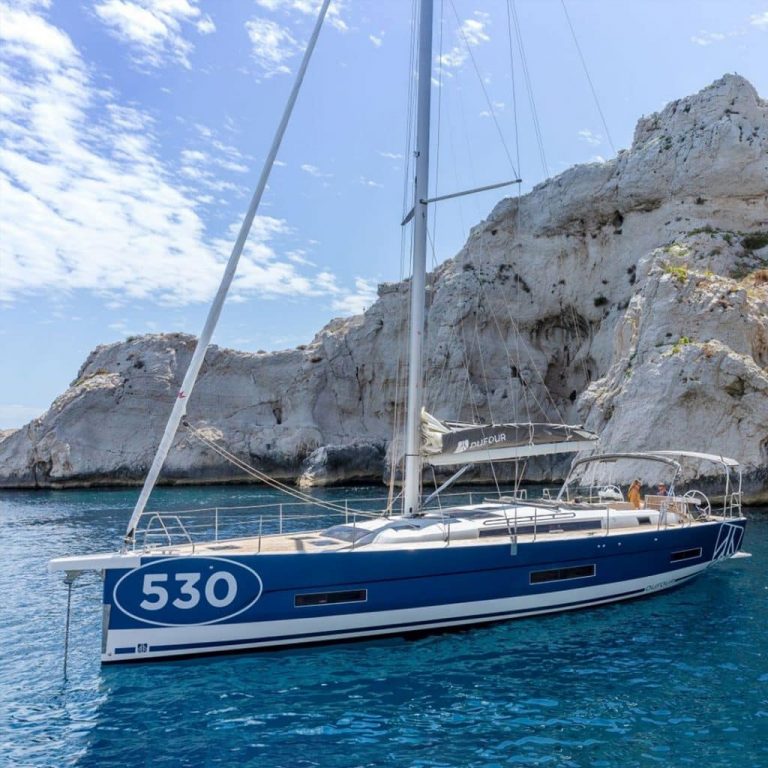 A blue sailboat in the water near the cliffs of Port Canto during the Cannes Yachting Festival 2023.