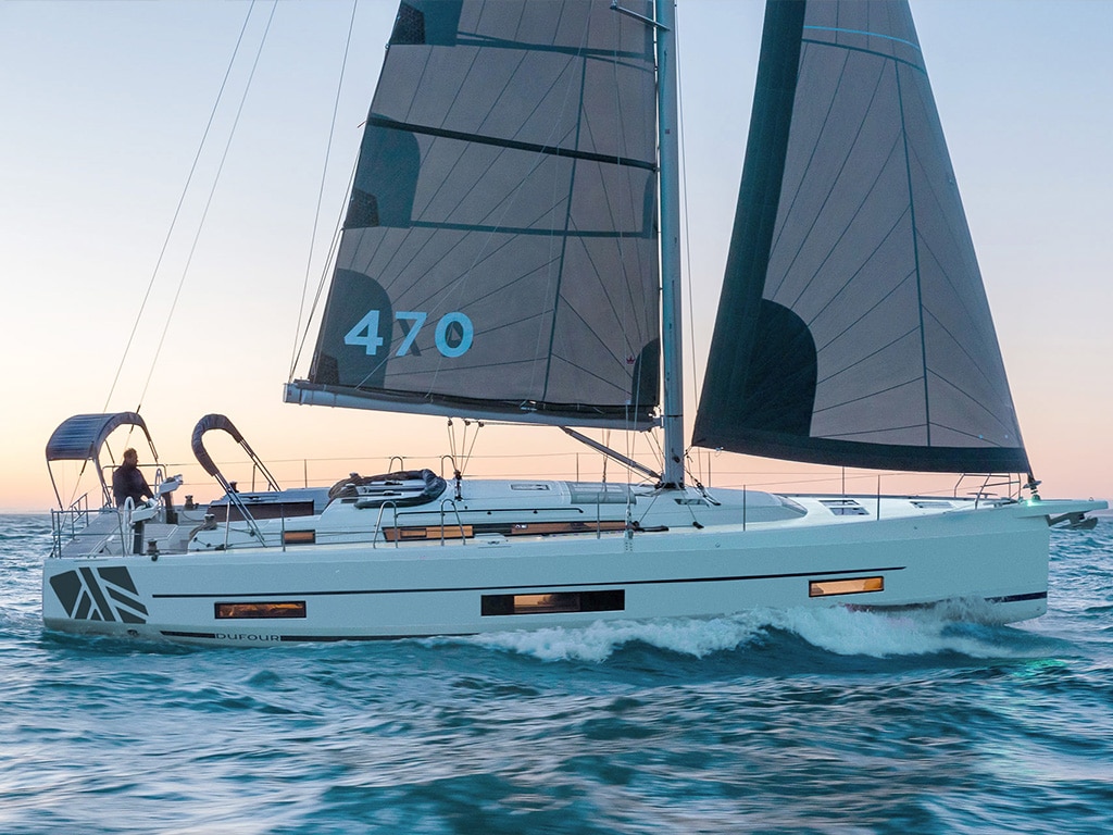 A Dufour 470 sailboat sails in the ocean at sunset. This type of boat is very popular in the yacht charter sector due to its outstanding characteristics.