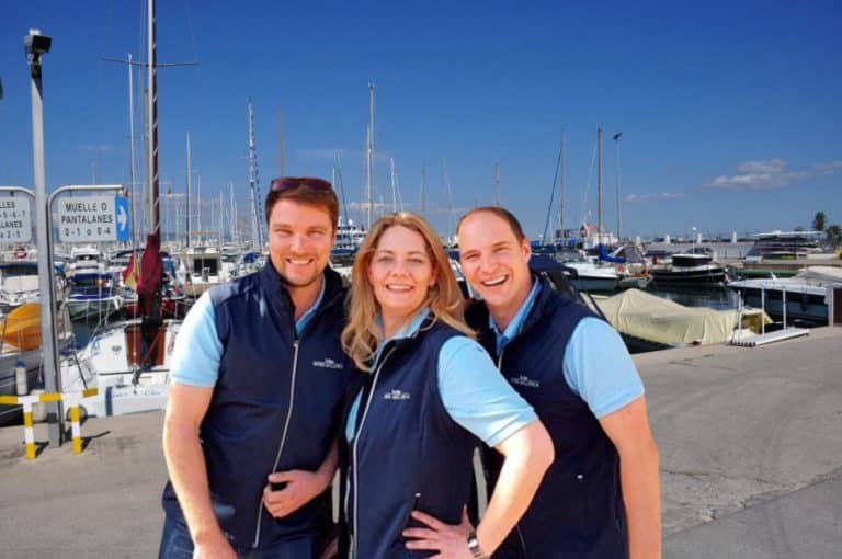 Three people pose for a photo in front of a marina with the Yates Mallorca Charter Team.