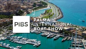 Aerial view of a yacht exhibition at the Palma International Boat Show with the coast and the buildings of the city in the background, with the logo of the event "PIBS" superimposed.