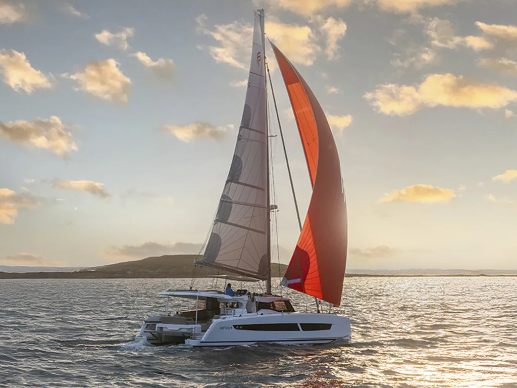 Luxuriöser Segelkatamaran auf dem Meer bei Sonnenuntergang. Segelboot mit rotem Segel und grauen Segeln.