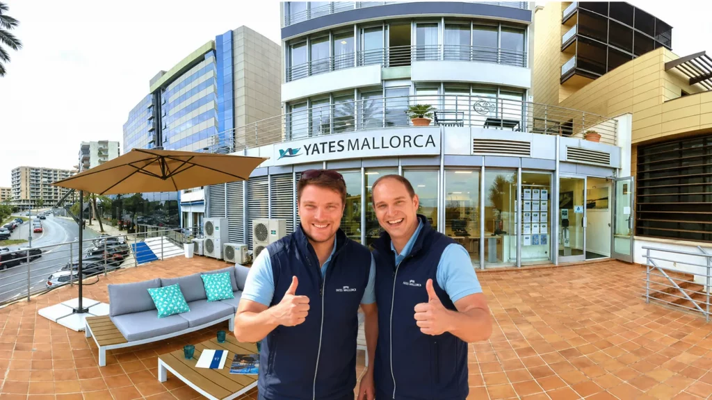 Yates Mallorca Team: Zwei Mitarbeiter mit Daumen hoch vor Bürogebäude. Yachtcharter auf Mallorca.